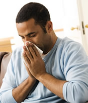 A man is sick with the flu and blowing his nose